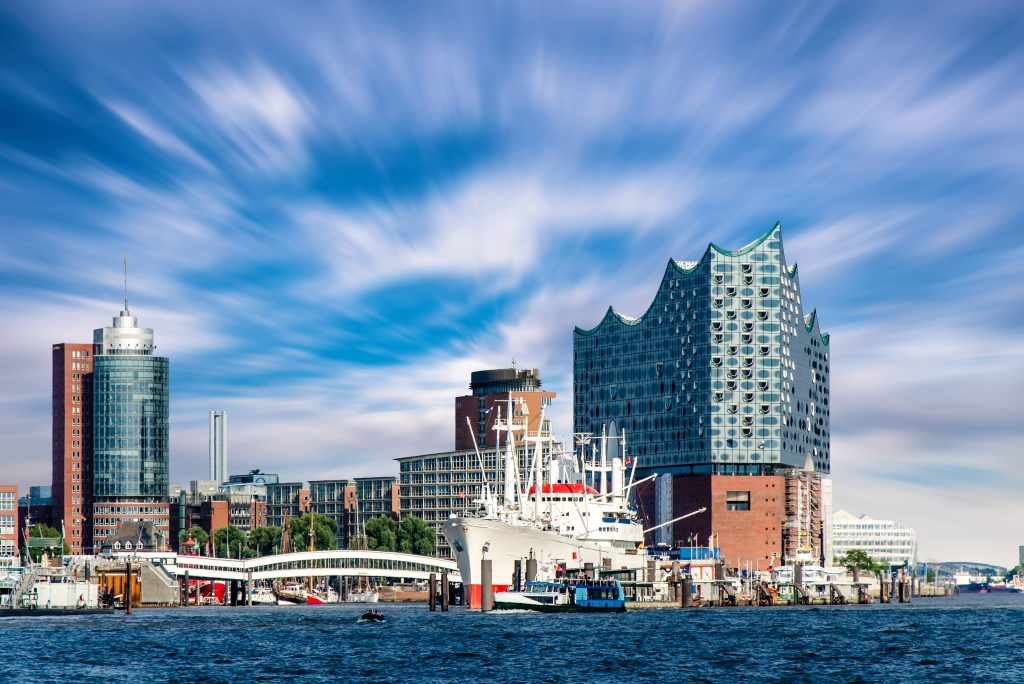 In der Glasfassade spiegeln sich Himmel und Wasser. Die Elbphilharmonie hebt sich eindrucksvoll vom roten Backstein des Speichers ab. Foto: StockAdobe/dietwalther