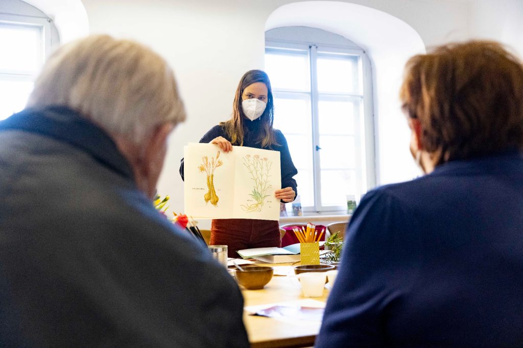 Kunsttherapeutin mit Maske zeigt ein Bild aus Gewürzfarben