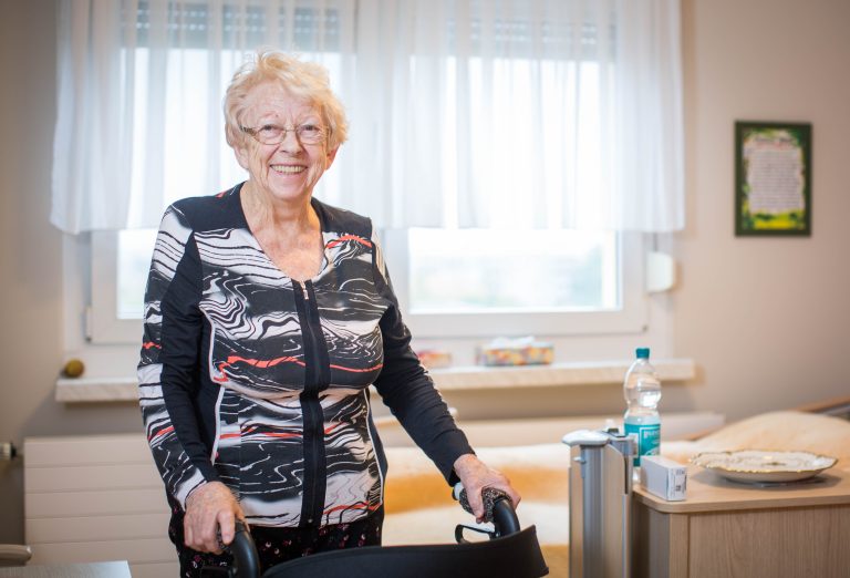 Dame steht im Zimmer mit Rollator.