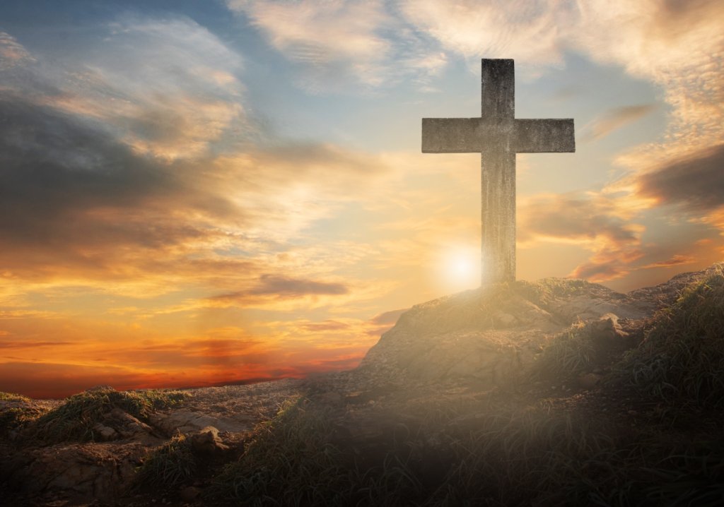 Ein Kreuz steht auf dem Berg und die Sonne geht unter.