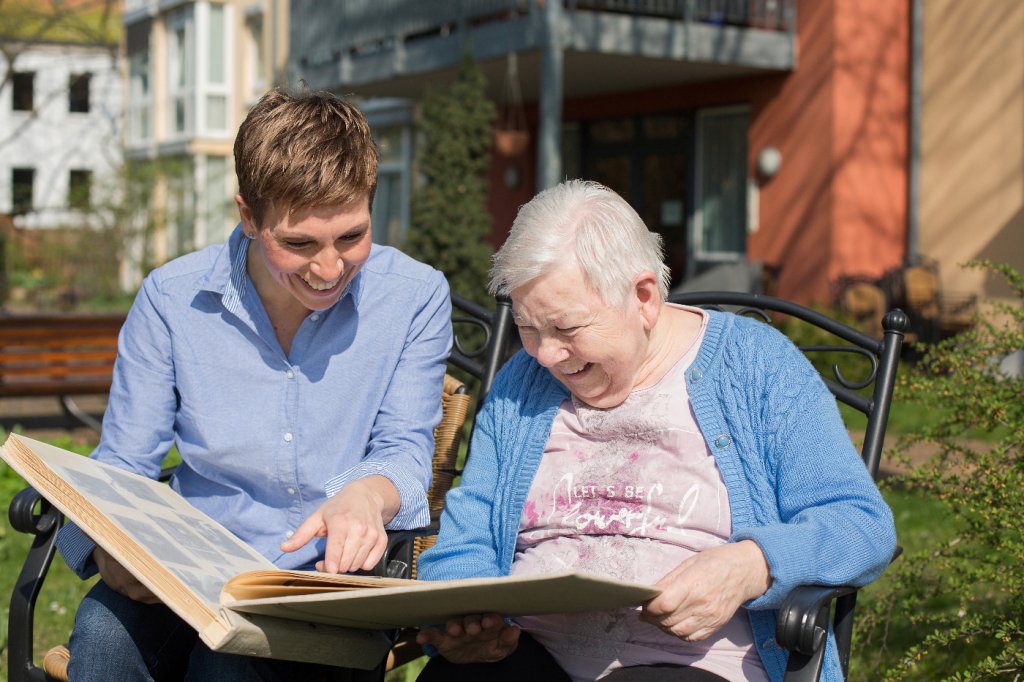 Seniorin und Seniorenassistentin blättern gemeinsam im Fotoalbum