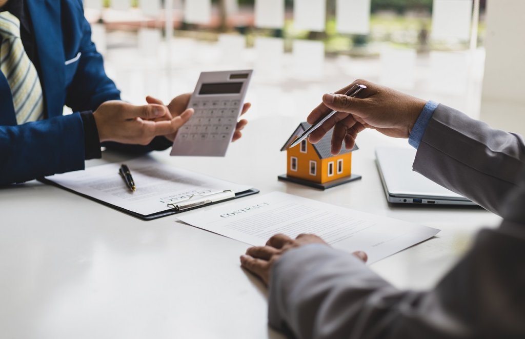 Ein Haus muss neu geschätzt werden. Zwei Menschen sitzen am Tisch und füllen gemeinsam die Unterlagen aus. Für die Kalkulation wird ein Taschenrechner