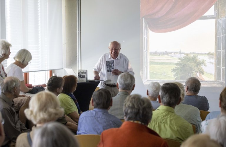 Vor aufmerksamen Zuhörern referiert der bekannte Kameramann Ernst Hirsch. Im Hintergrund: Eine Leinwand, die ein offenes Fenster mit Blick in die Landschaft zeigt.