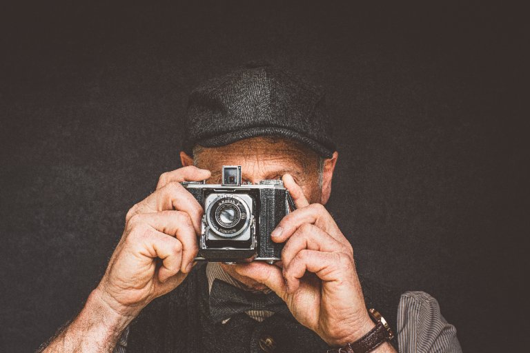 Älterer Herr oder Senior mit Hut schaut durch Fotoapparat.