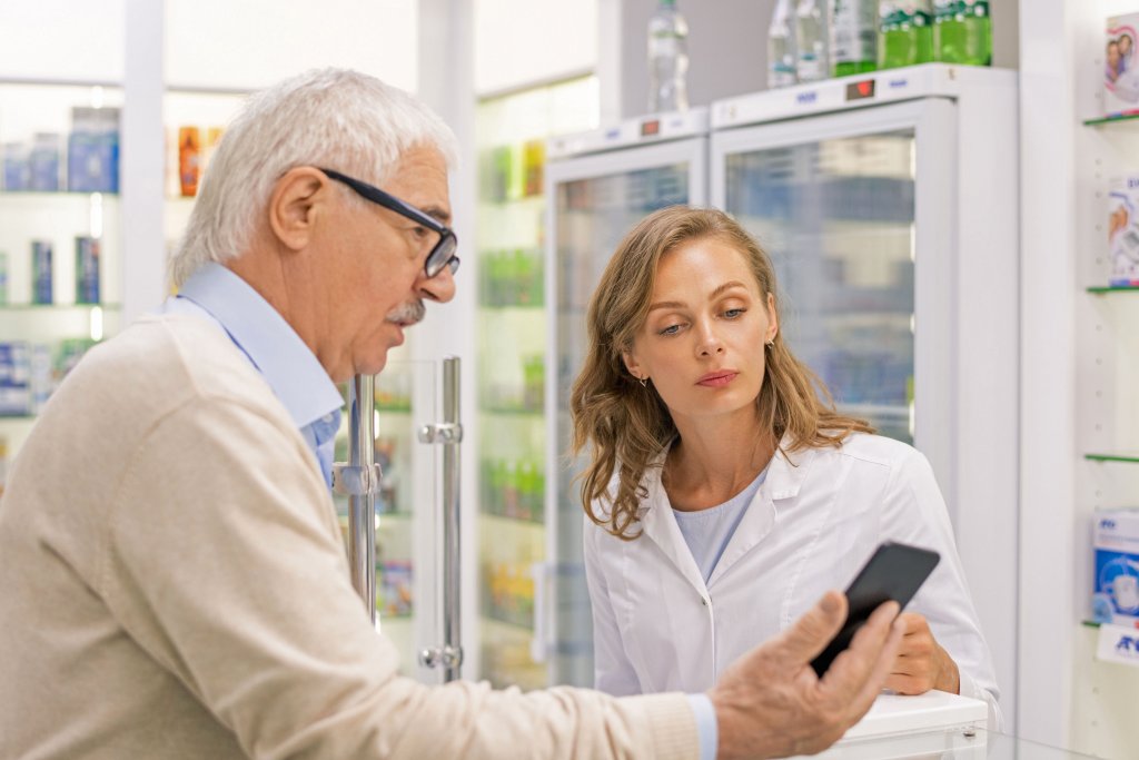 Ein Senior lässt sich in einer Apotheke beraten und zeigt der Apothekarin sein Smartphone. Foto: DJD/gematik/pressmaster - stock.adobe.com