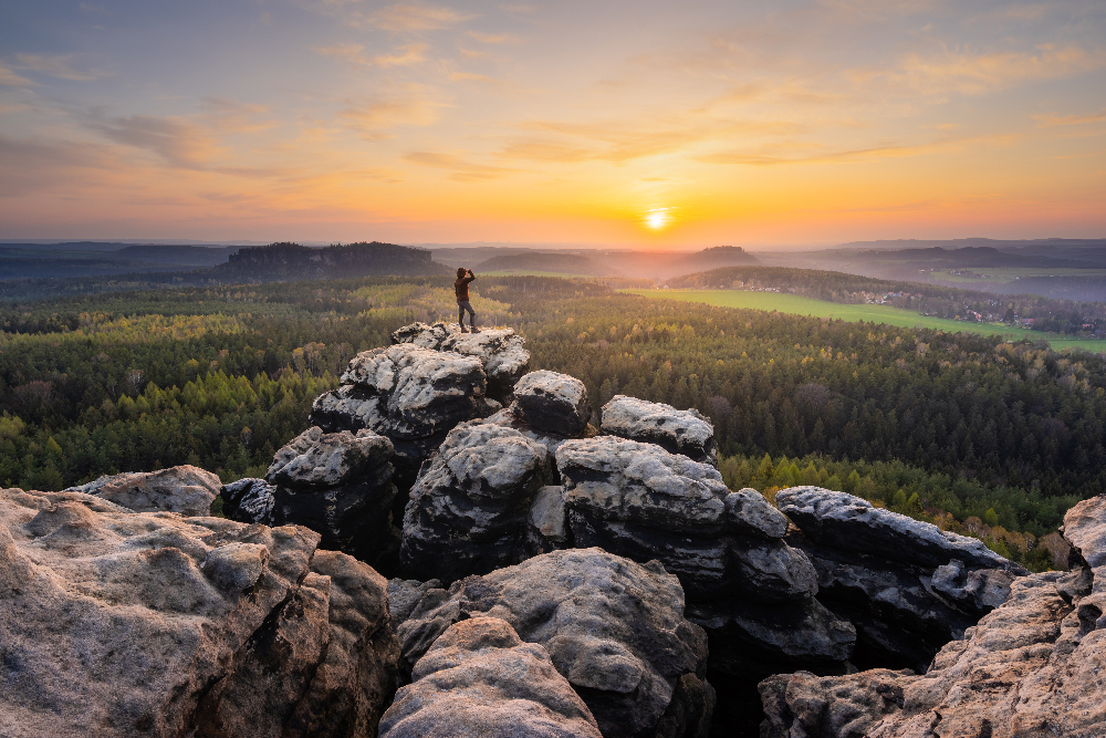 Blick zum Pfaffenstein im Abendlich der Sächsischen Schweiz mit einem Wanderer auf einer Bergspietze im Hintergrund