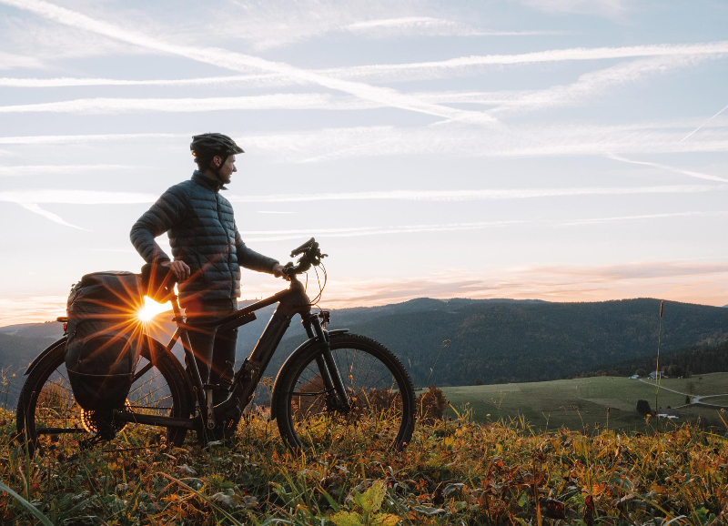 E-Bike Fahrer ist vom Rad abgestiegen und schaut in das Abendlicht in einer Landschaft.